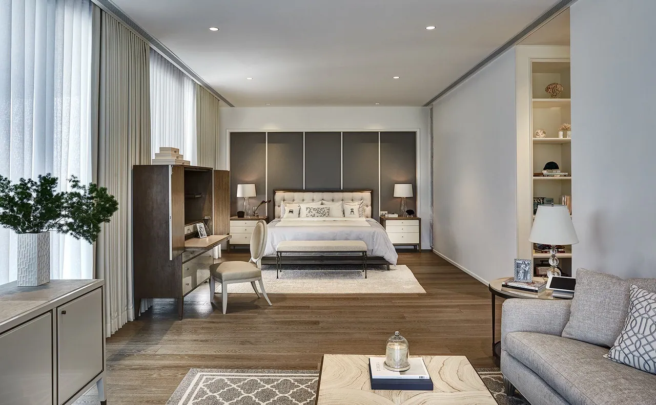 Master bedroom at Baan Krungthep Kritha — an upholstered bed against a panelled grey headboard wall, with a sitting area, oak flooring and full-height sheer curtains.