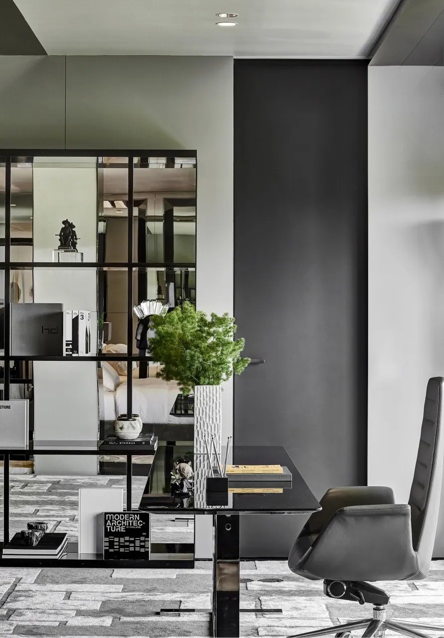 Desk at Baan Krungthep Kritha set behind a blackened steel grid screen, with a leather task chair and a view through the glazed partition to the bed beyond.