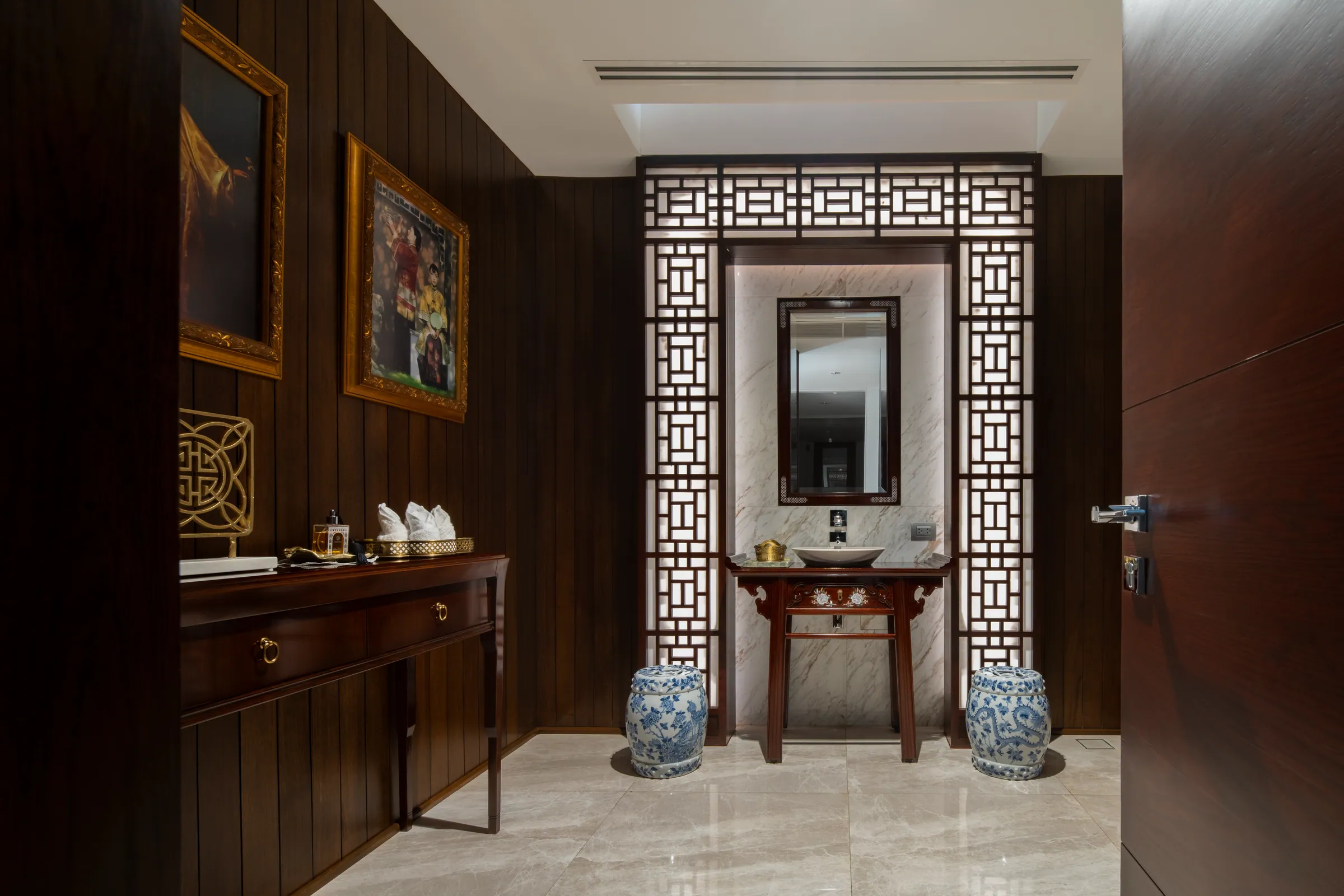 Foyer of Khon Kaen Residence — dark teak panelling, polished cream marble floor, two cobalt porcelain garden stools, gilt-framed mirror.
