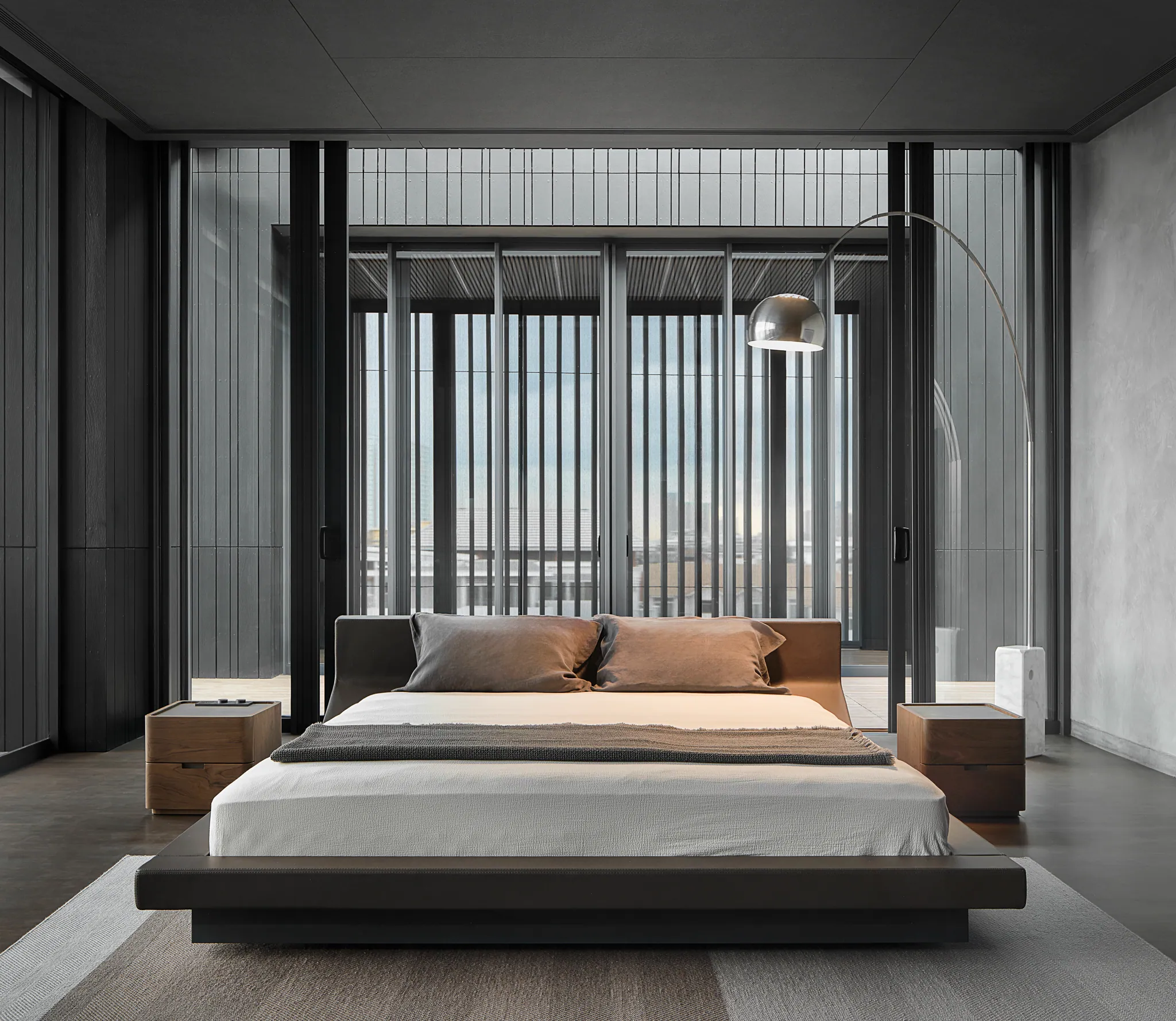 Dark bedroom at Black Box Project — amber wood wall, black leather chaise, marble accent, gallery lighting.