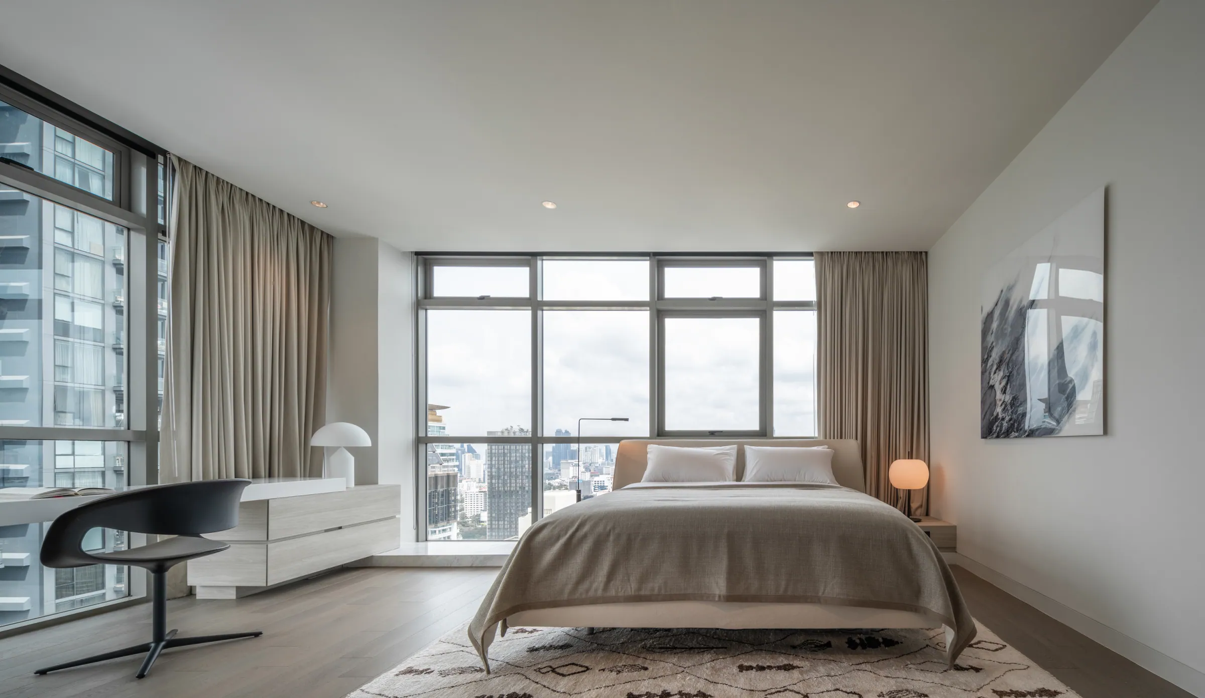 Guest bedroom at Madison Penthouse — taupe bed facing corner windows, a patterned rug and a white lacquer desk run.