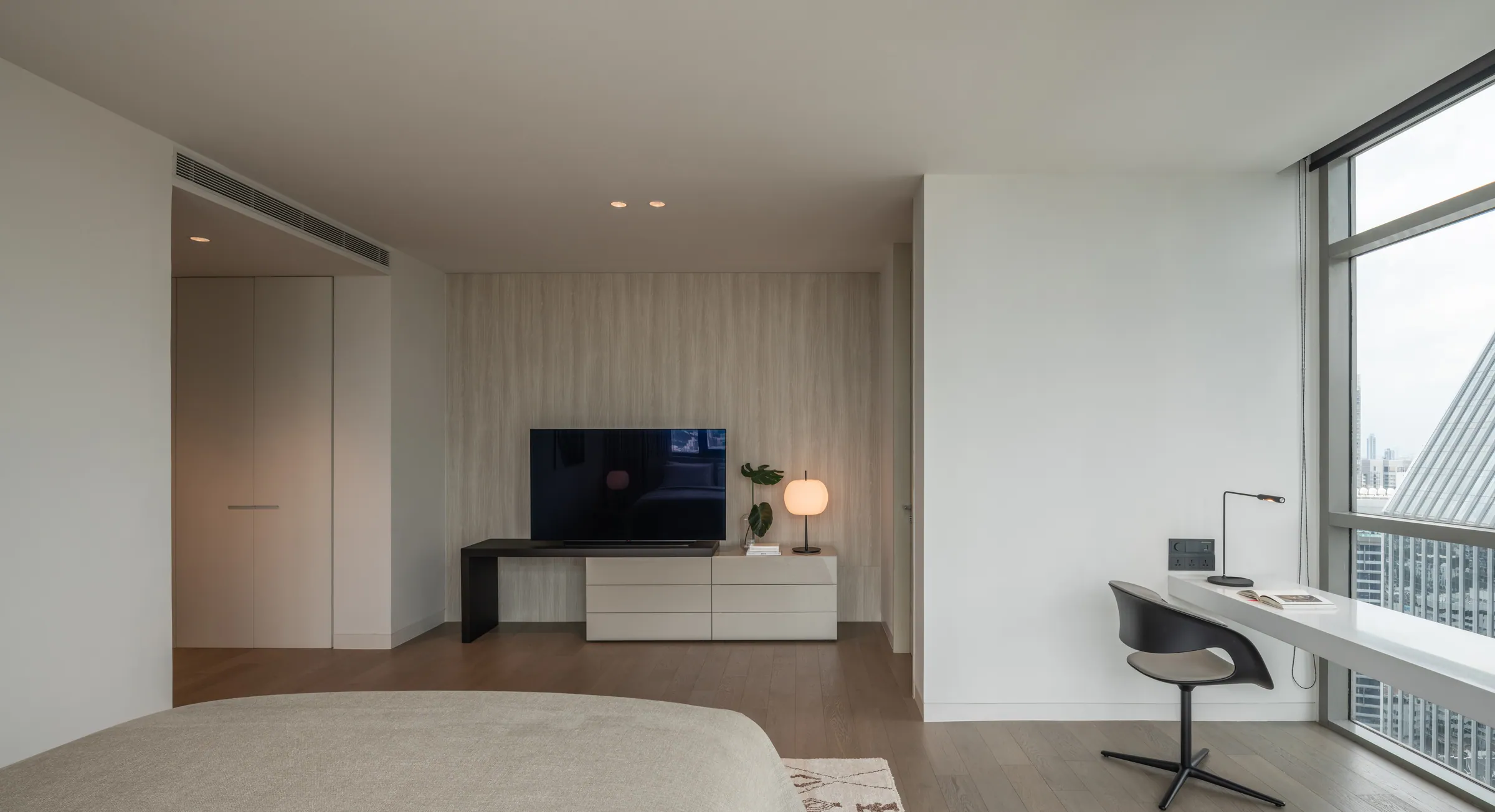 Guest bedroom at Madison Penthouse — media console and desk along the pale stone wall, seen from the bed.
