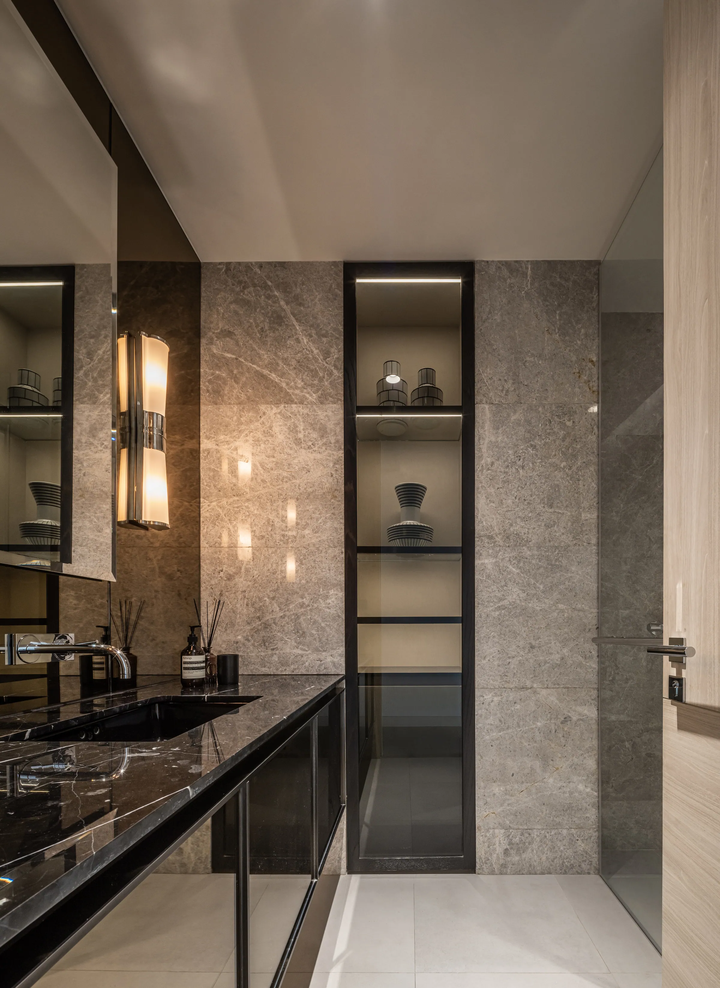 Guest bathroom at Madison Penthouse — grey marble slab wall, backlit black-framed niches and a black stone counter.
