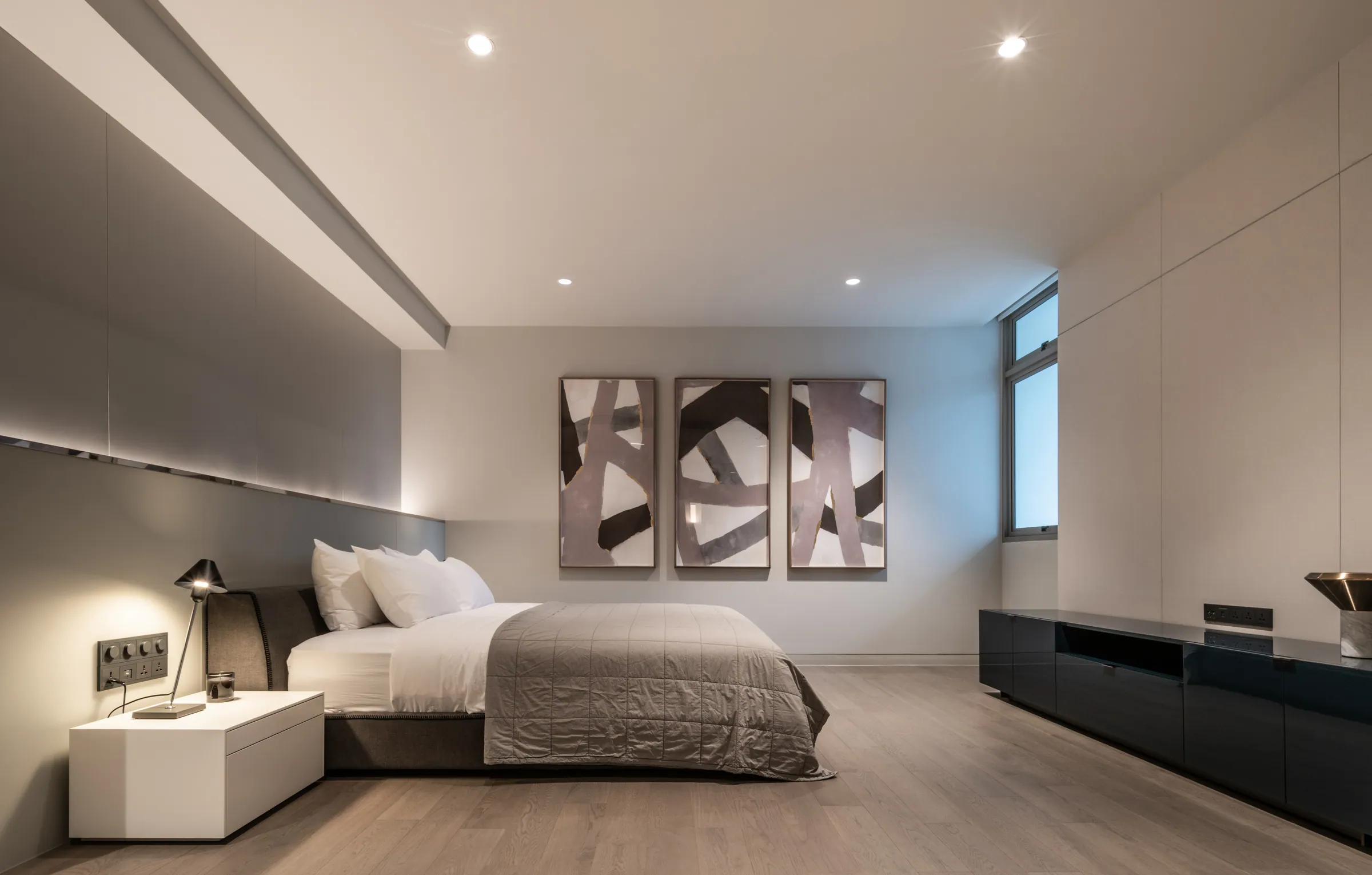 Third bedroom at Madison Penthouse — an abstract triptych above the bed, a black media console and a stepped ceiling with cove lighting.
