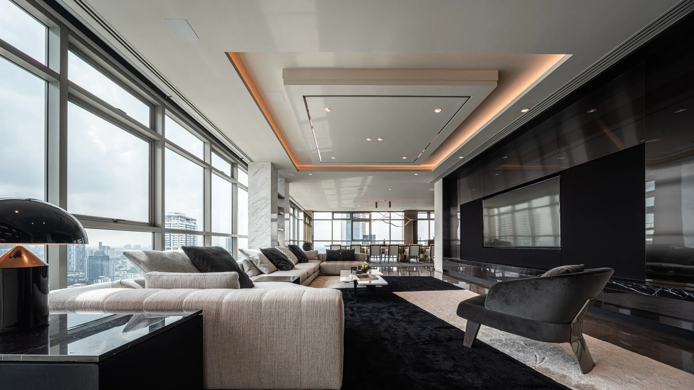 Living room at Madison Penthouse — deep sectional on a black rug, dark stone media wall, cove-lit stepped ceiling and panoramic city glazing.