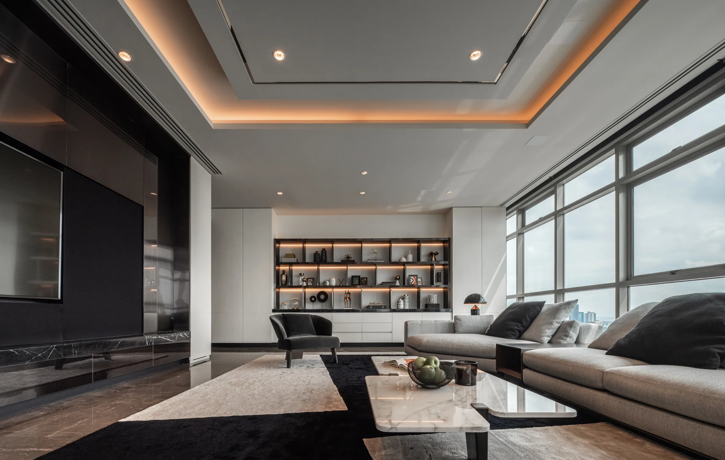 Living room at Madison Penthouse from the dining end — marble coffee table, book-lined display wall, dark feature wall and perimeter cove lighting.
