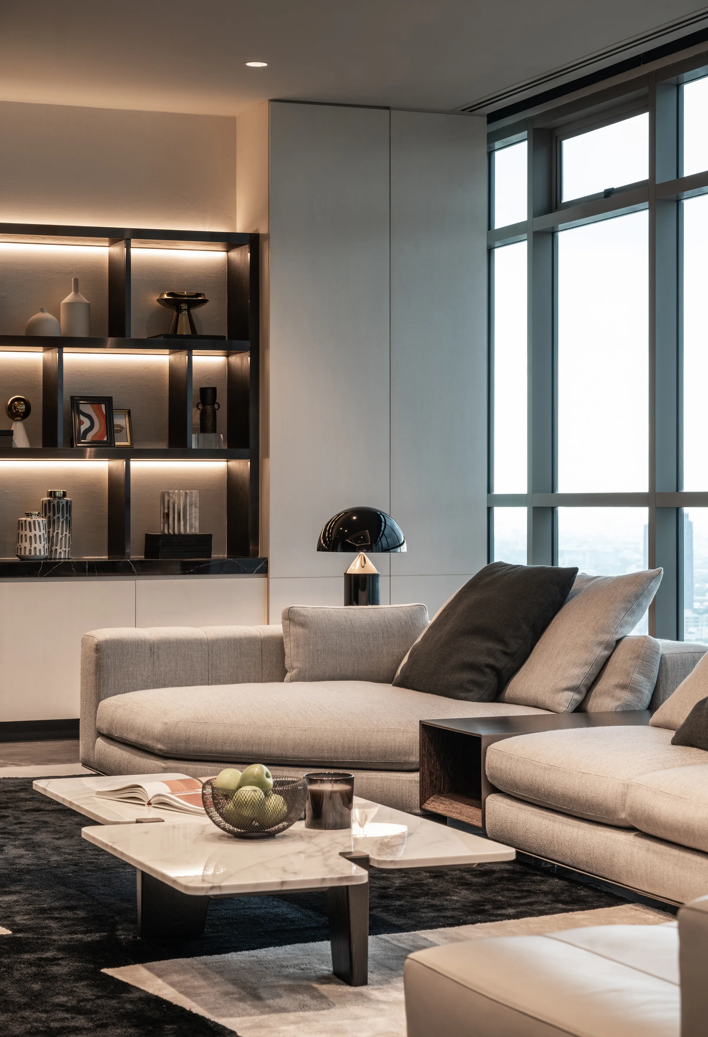 Sofa corner at Madison Penthouse — cream sectional with charcoal cushions and a black glass table lamp on a brass base.