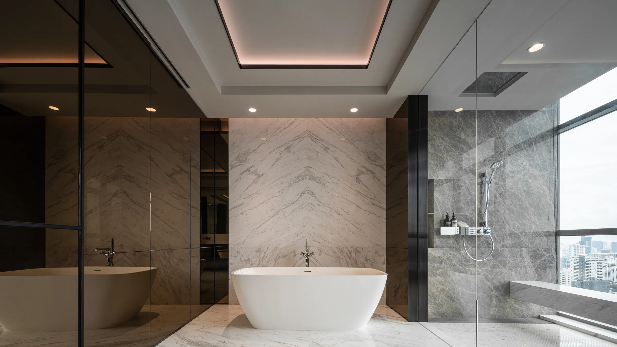 Master bathroom at Madison Penthouse — oval freestanding tub centred on a book-matched marble wall with a floor-mounted filler.