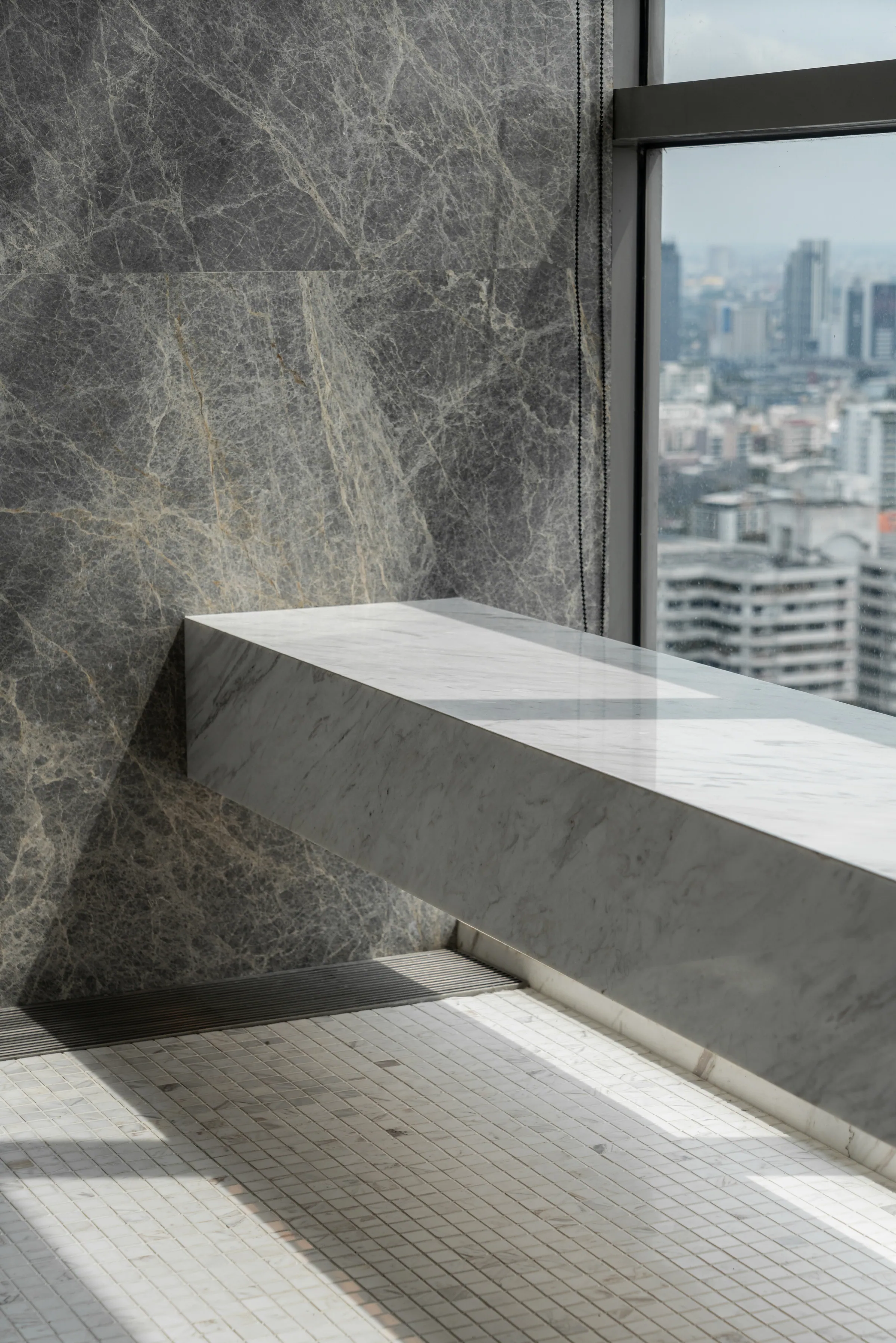 Marble detail at Madison Penthouse — a cantilevered stone bench against a grey-green book-matched slab wall.