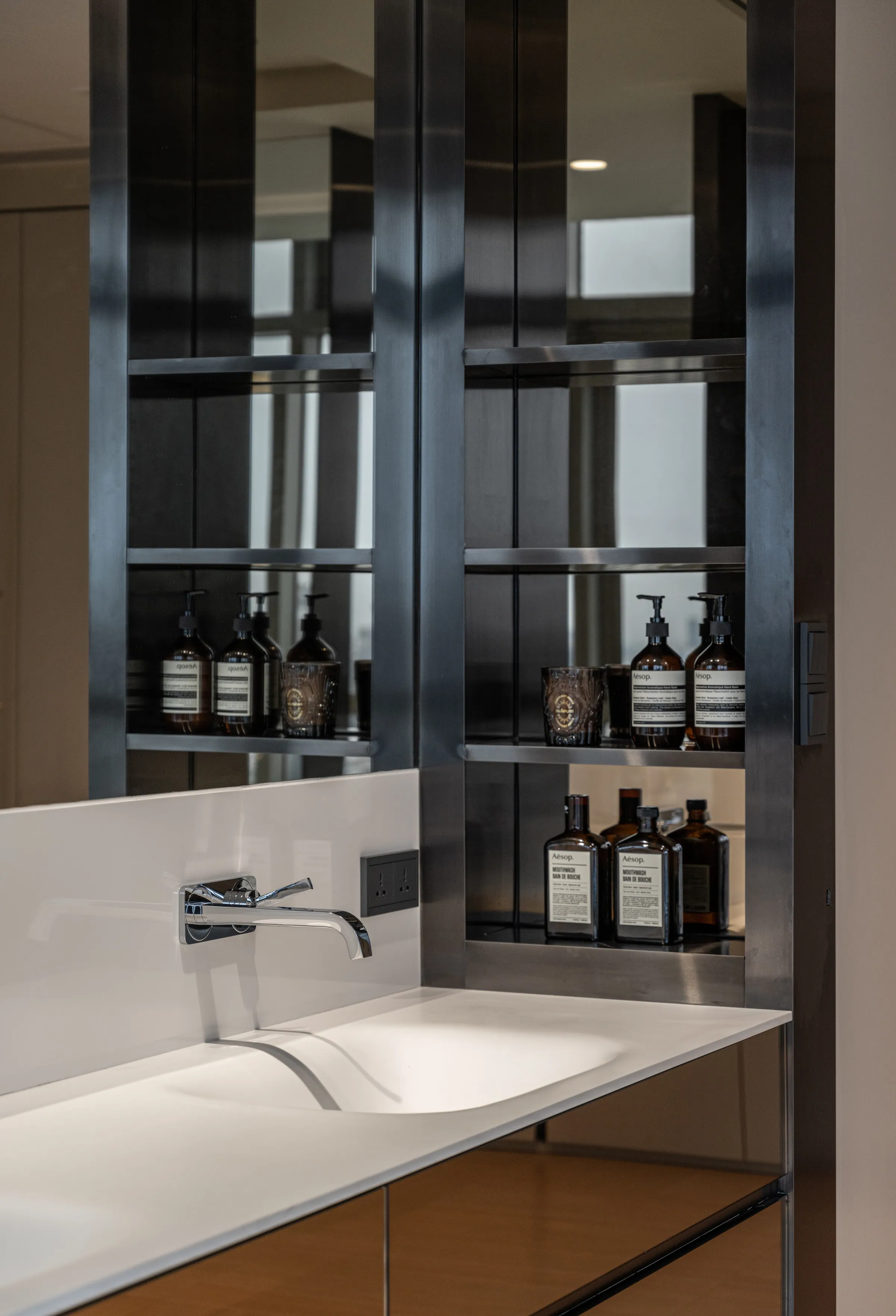 Bathroom shelving detail at Madison Penthouse — apothecary bottles on blackened steel shelves beside a wall-mounted chrome spout.