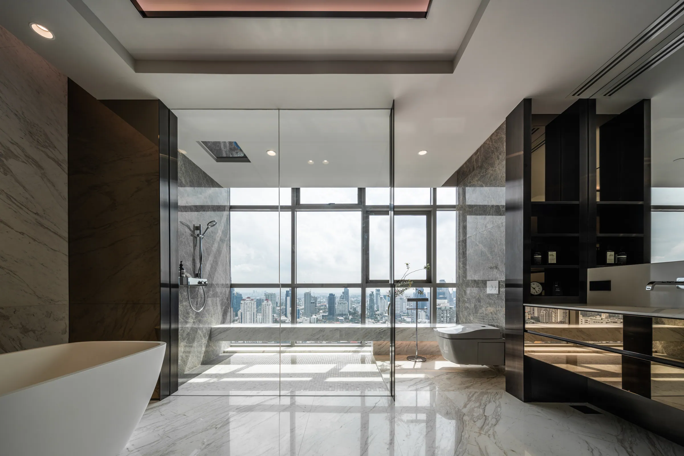 Master bathroom at Madison Penthouse — freestanding tub against floor-to-ceiling glass with the Bangkok skyline beyond.