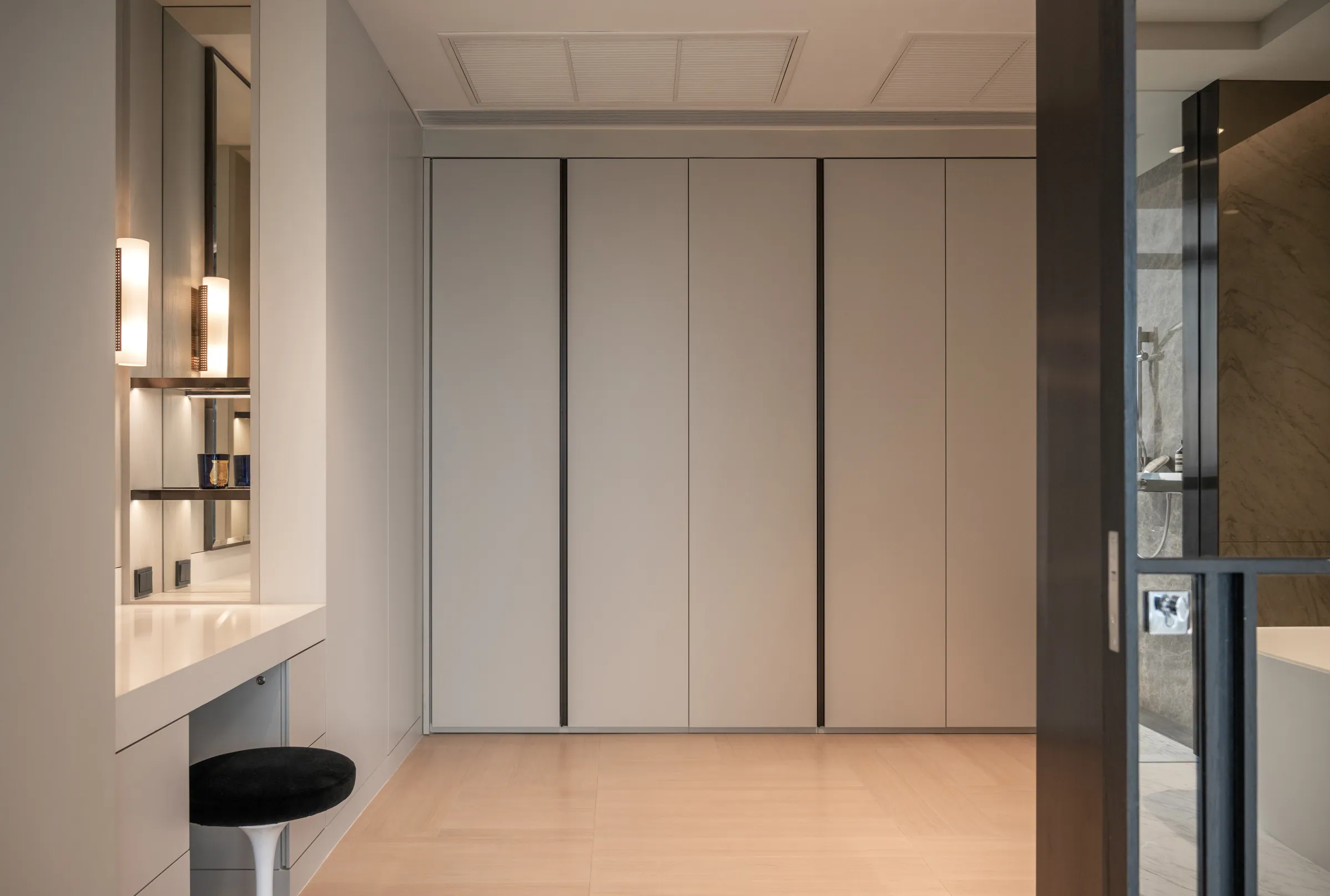 Dressing area at Madison Penthouse — lit vanity mirror, pale full-height wardrobe doors and a black round stool.
