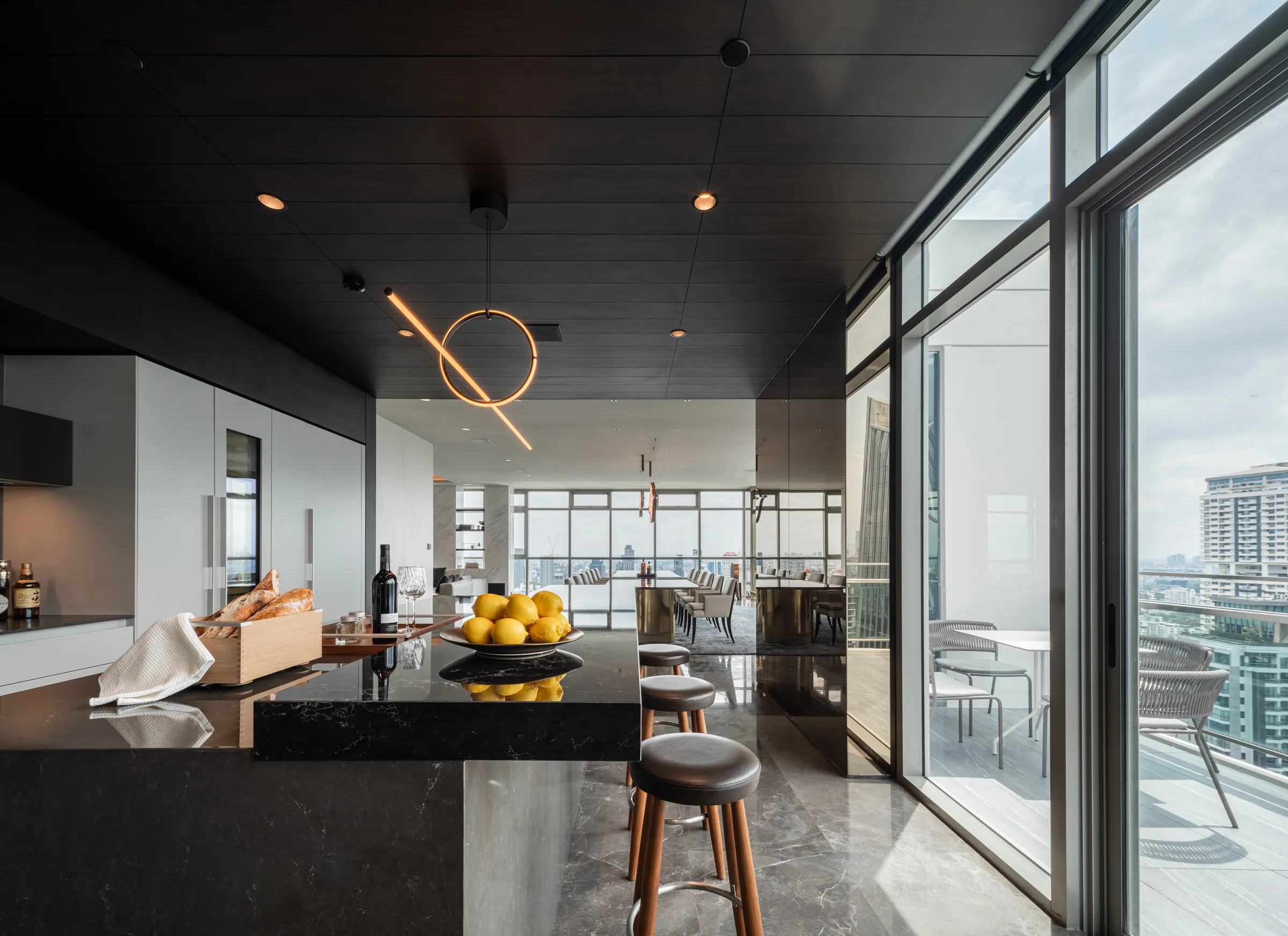 Pantry bar at Madison Penthouse — dark stone island with timber stools, looped filament pendant and sliding glass out to the terrace.