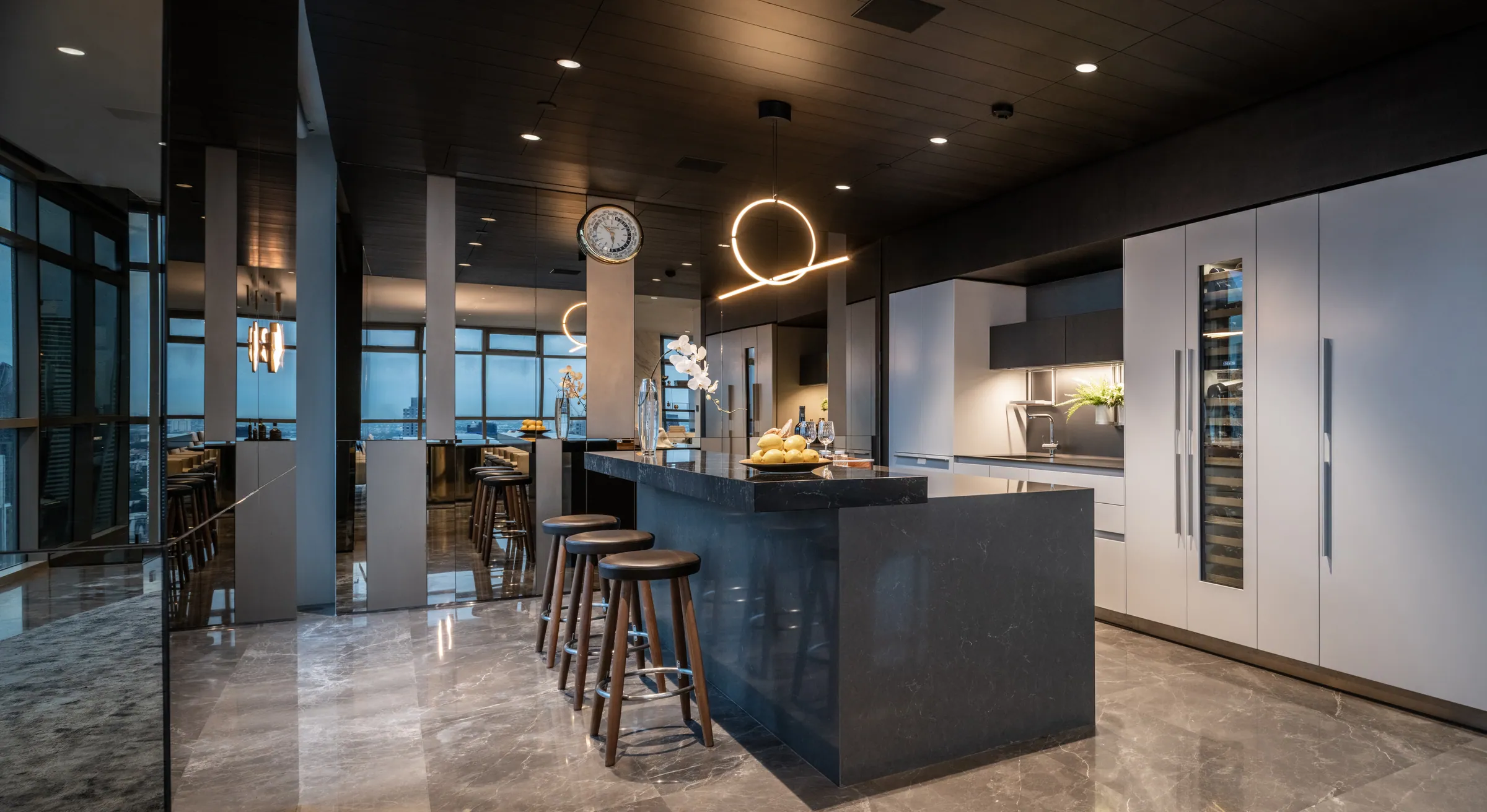 Pantry at Madison Penthouse — dark island with four stools, integrated wine cabinet, pale joinery and a looped filament pendant.