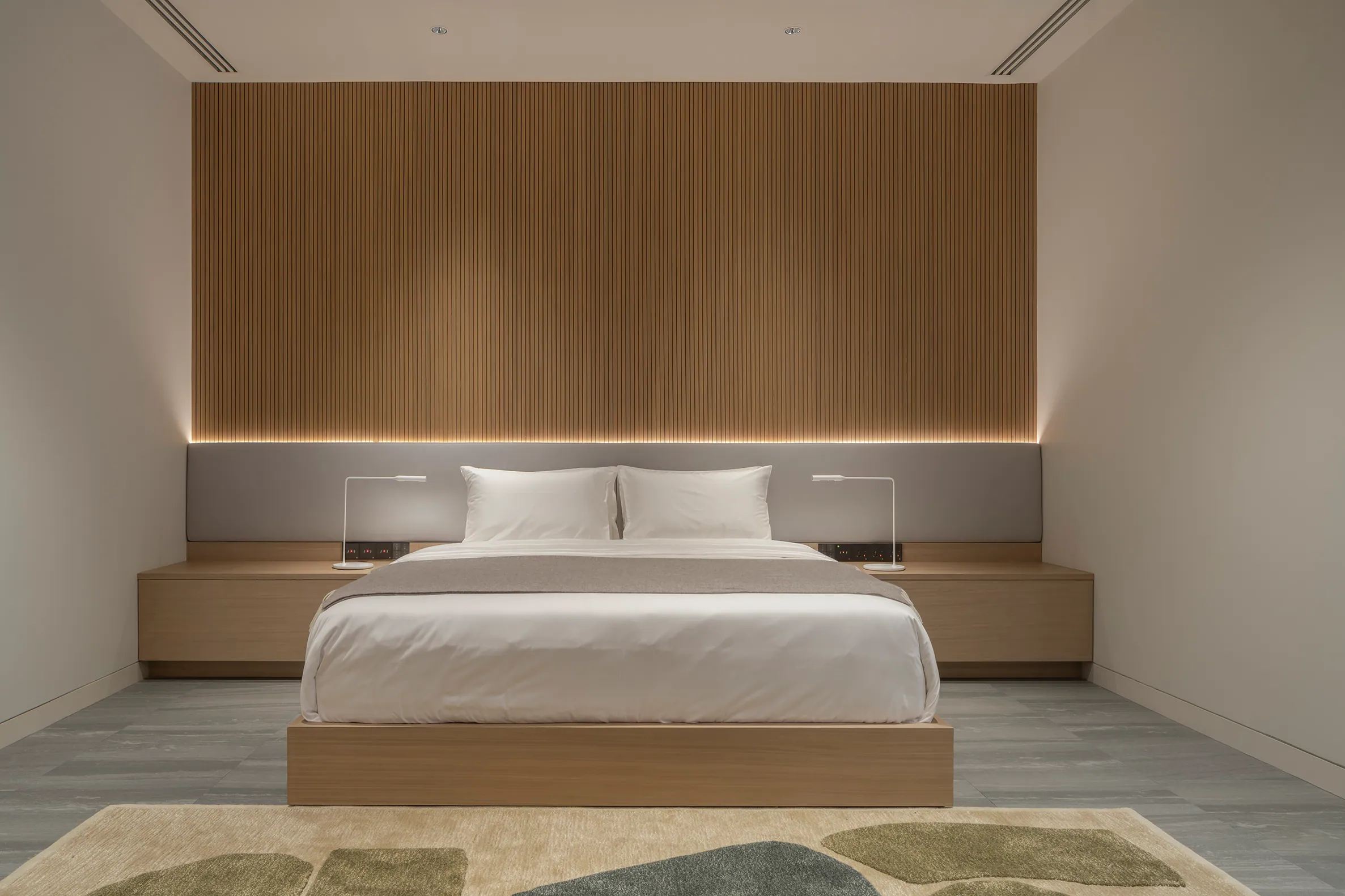 Master bed headwall detail — vertical wood slats with integrated ambient light.