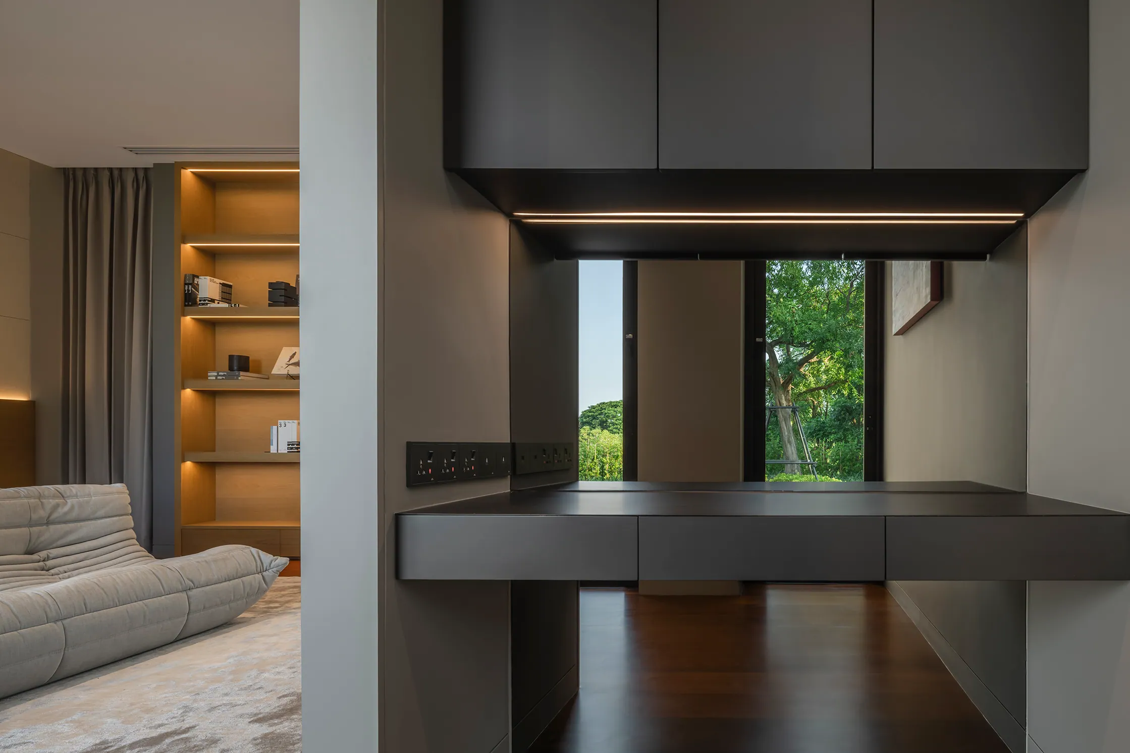 Master bedroom at Water House — minimal platform bed, warm wood headwall with vertical slats, lounge chair, terazzo rug.