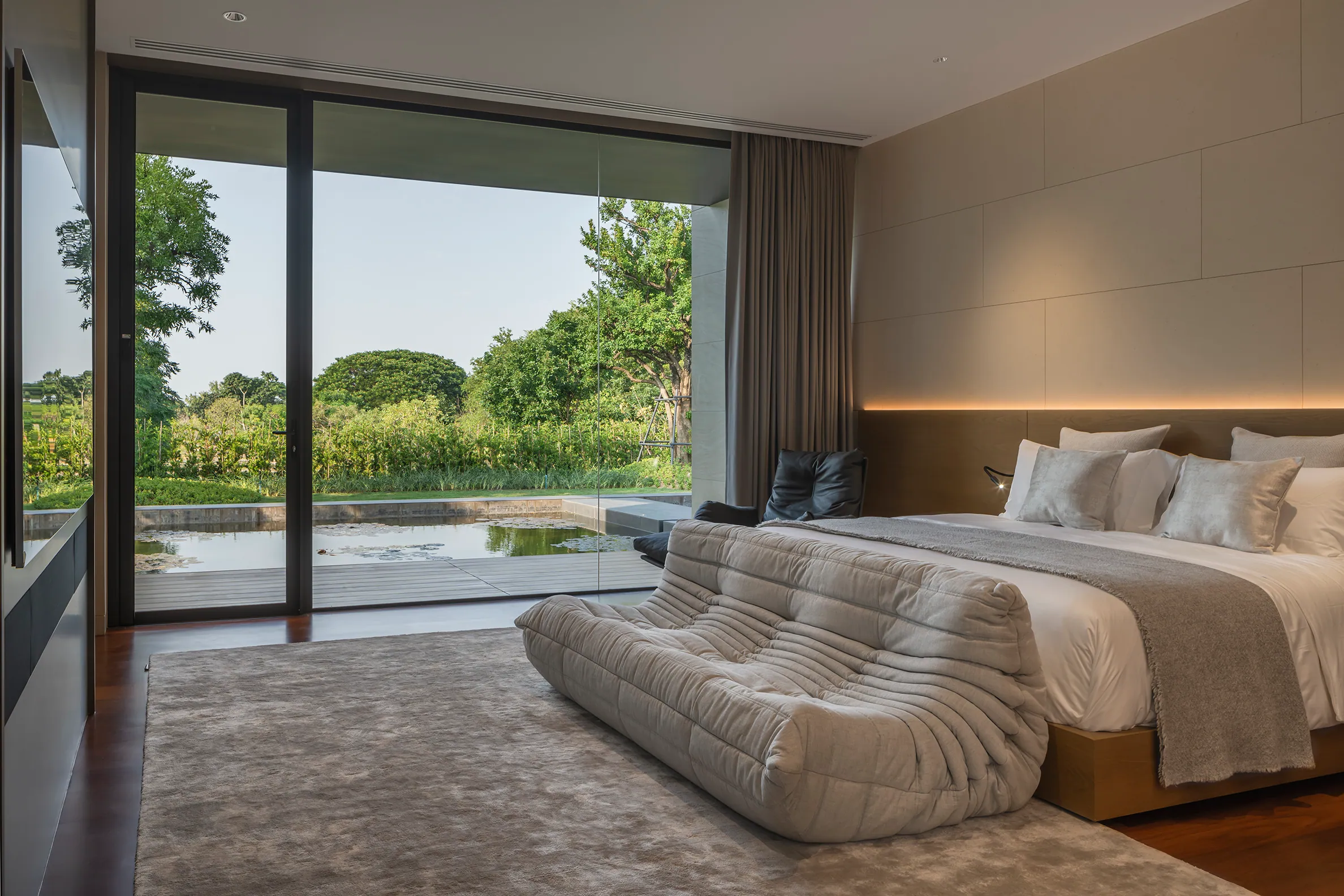 Guest bedroom at Water House — minimalist platform, pool-facing glass wall, integrated lounge.